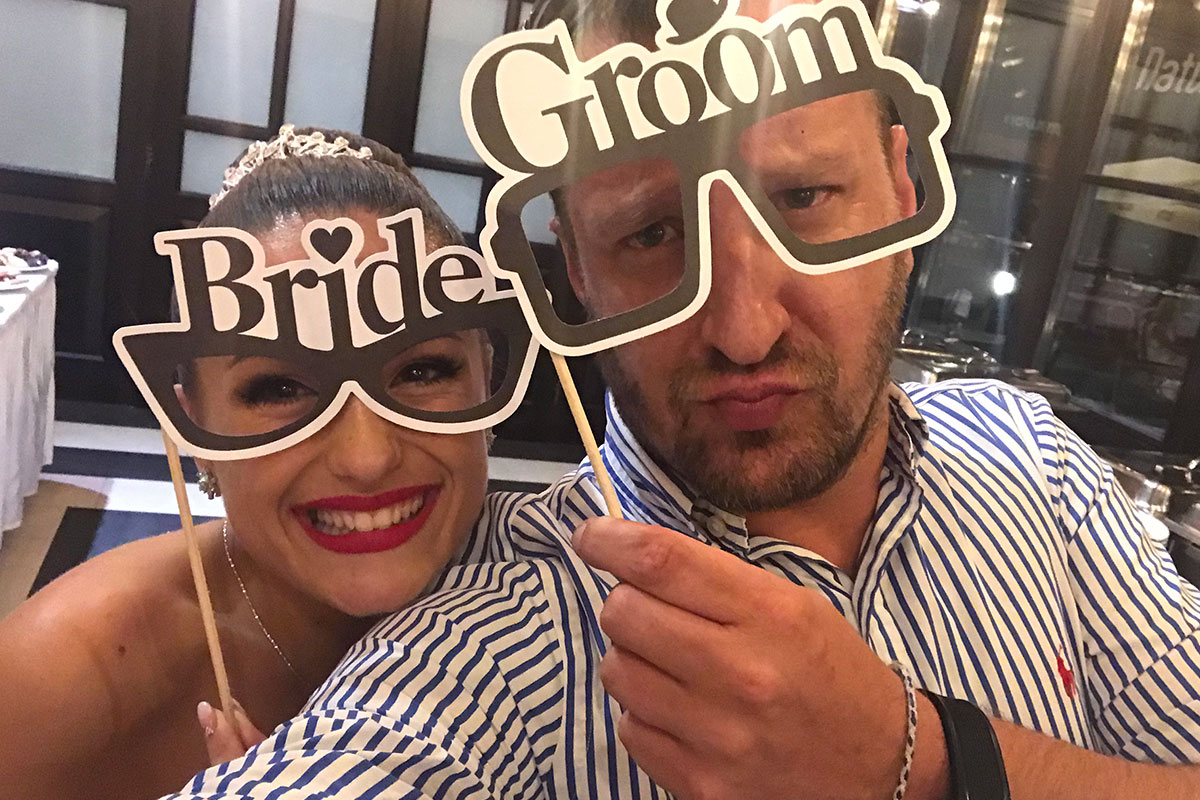 Menyasszony és vőlegény vicces „Bride” és „Groom” feliratú szemüveggel szórakozik az esküvői bulin